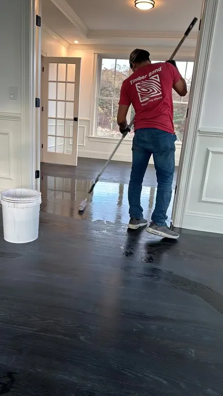 YK United Builders craftsman applying the finish coat to a hardwood floor